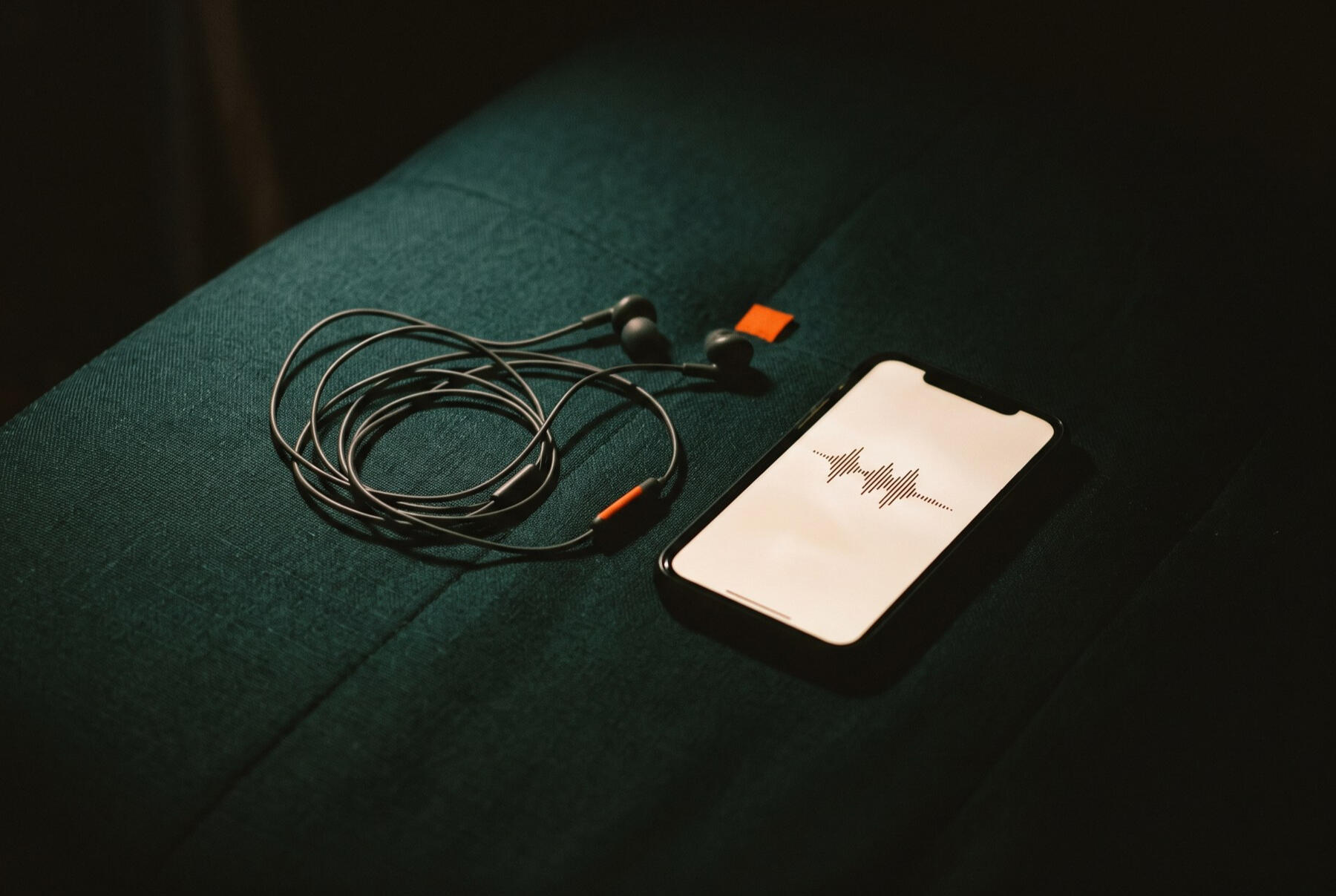 Audífonos sobre una tela verde oscuro junto a un celular con una onda de audio